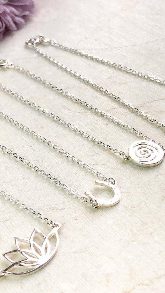 four sterling silver bracelets with different symbolic meanings laid out side by side on a cream stone with a purple flower in the background