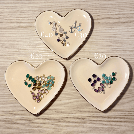 a selection of charms for permanent/welded jewellery laid out on  peach heart shaped dishes with a gold trim