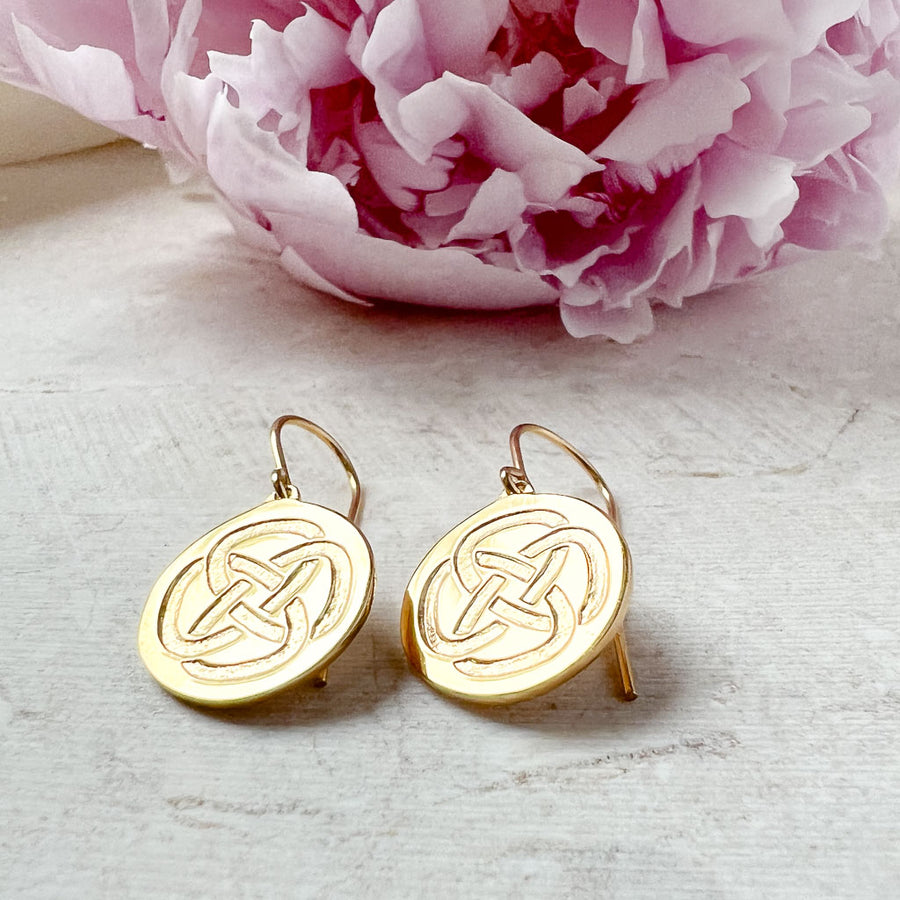 dara knot gold plated drop earrings resting on a stone with a pink flower in the background