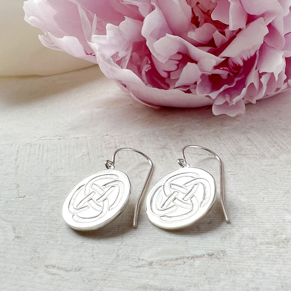 sterling silver drop earrings symbolising strength resting on a stone with a pink flower in the background