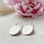 sterling silver drop earrings symbolising strength resting on a stone with a pink flower in the background