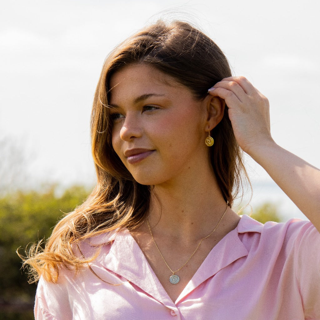 a woman staring into the distance  wearing a gold plated dara knot strength necklace with matching earrings