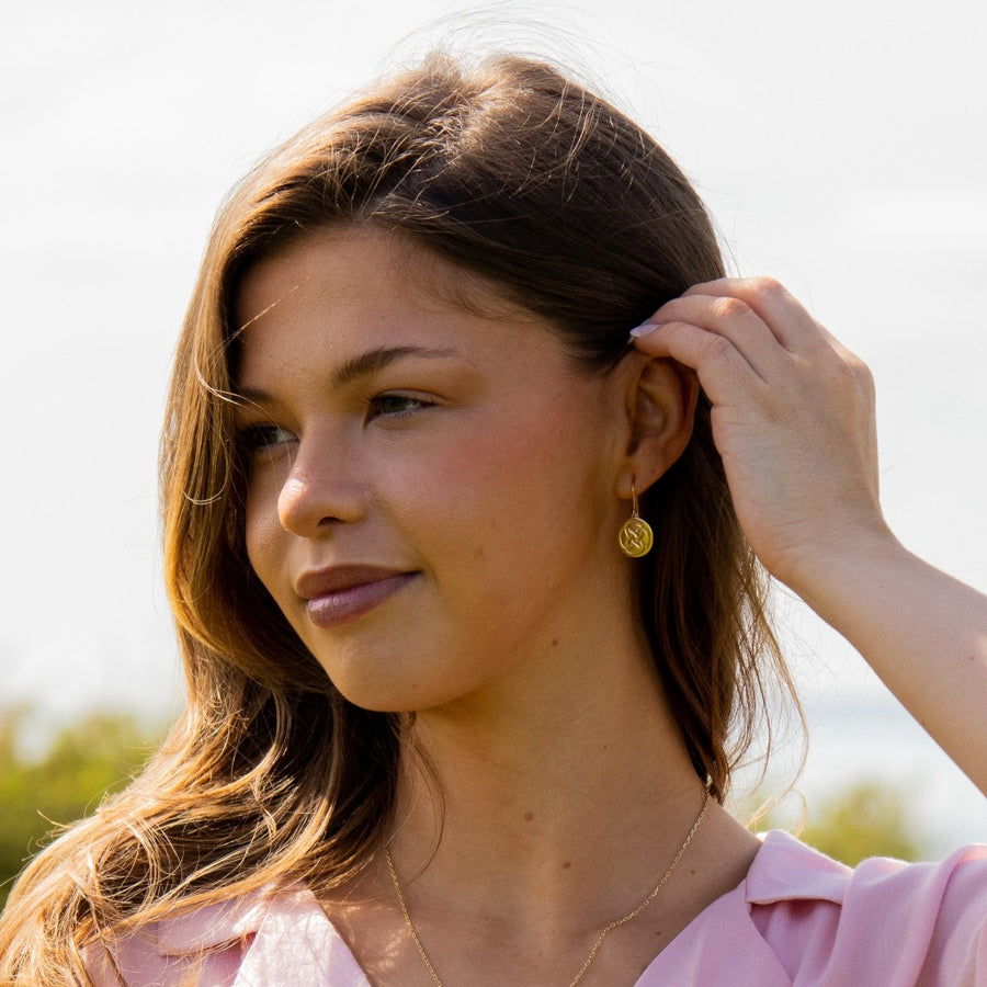 a woman tucking her hair behind her ear showcasing gold plated dara knot drop earrings 